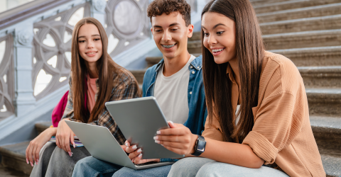 Scholieren zitten bij elkaar op een trap en bekijken een leuk bericht op laptop